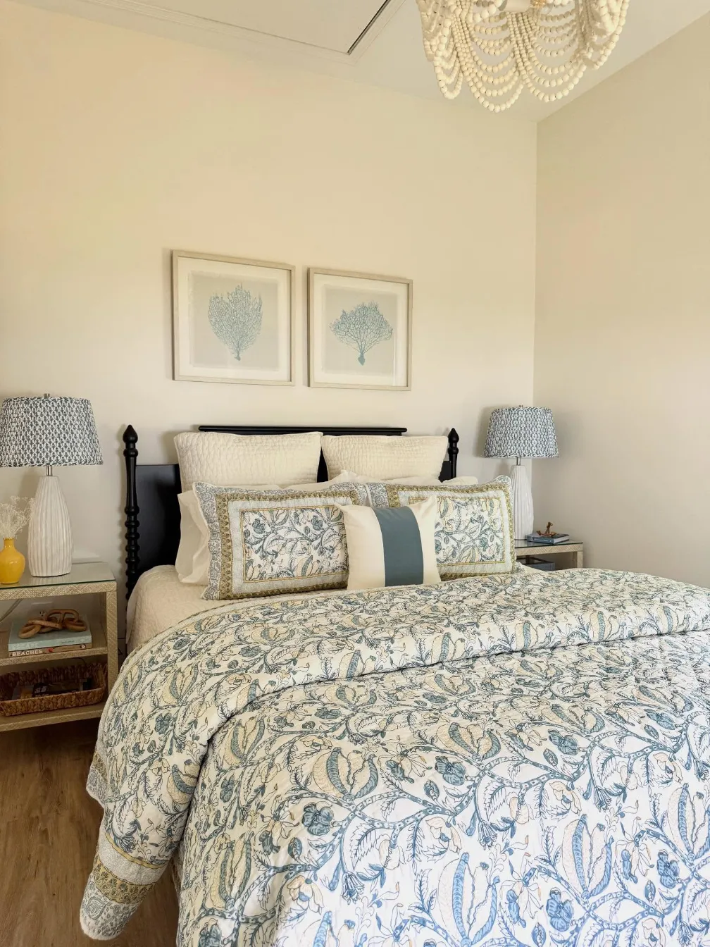 Coastal bedroom with blue and white patterned bedding, framed coral prints and a beaded chandelier