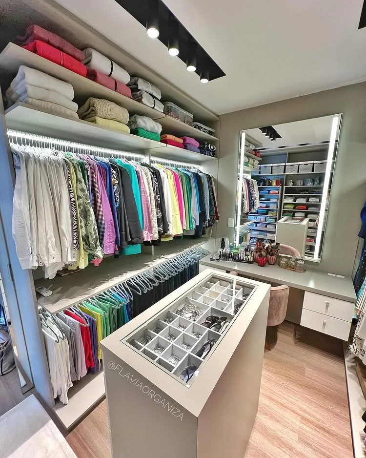 A luxurious walk-in closet organization idea featuring color-coded hanging clothes, a jewelry island, and a built-in vanity