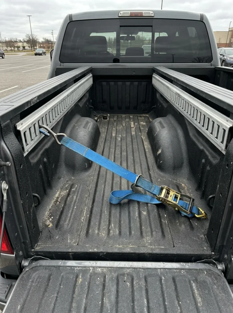 Truck bed fitted with metal side rails and a blue ratchet strap attached to clips inspired by e track bed ideas