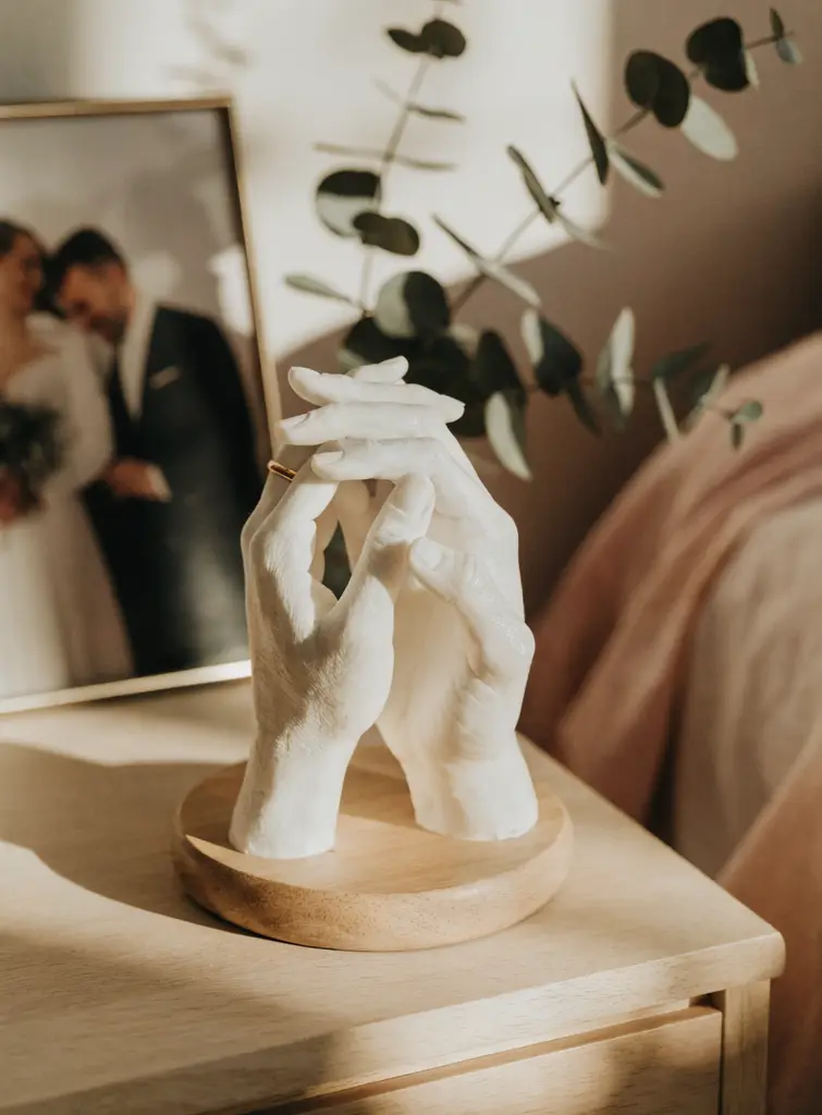 Couple wax hand ideas showing two interlocked white wax hands with a gold ring on a wooden pedestal