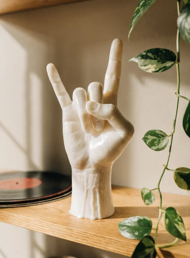 White rock on wax hand sculpture on an oak shelf beside vinyl records and a trailing pothos plant