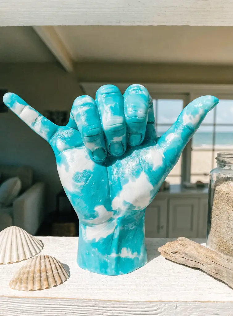 Turquoise marbled hang loose wax hand on a coastal shelf with seashells and driftwood